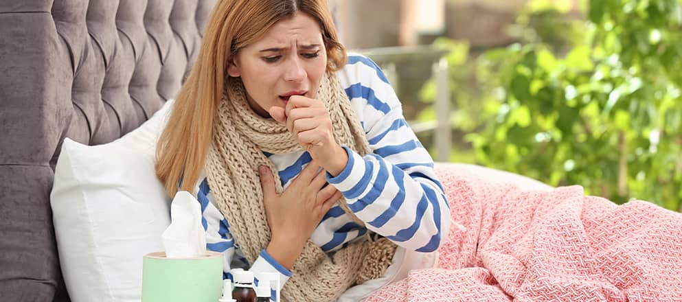 Vrouw ligt in bed onder roze deken en moet erg zwaar hoesten