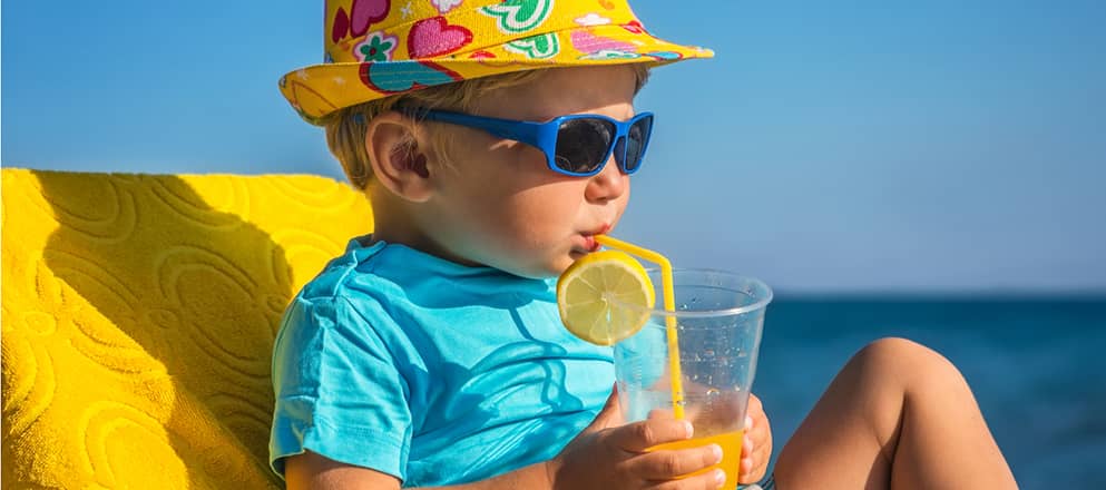 Jongen van 3 jaar drinkt limonade in de zon op het strand.
