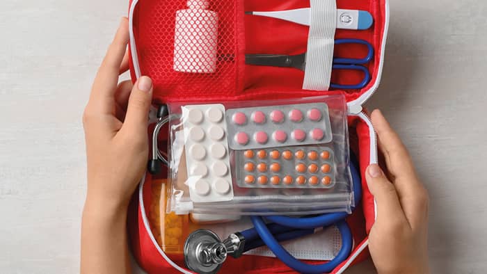 Rode medicijntas met onder andere verschillende pillenstrips, een thermometer en een stethoscoop