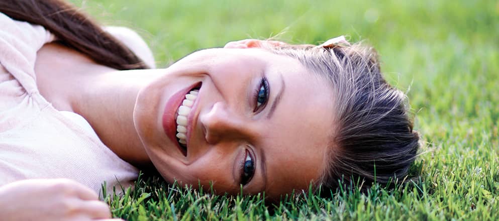 Een jonge vrouw met hooikoorts ligt lachend in het gras