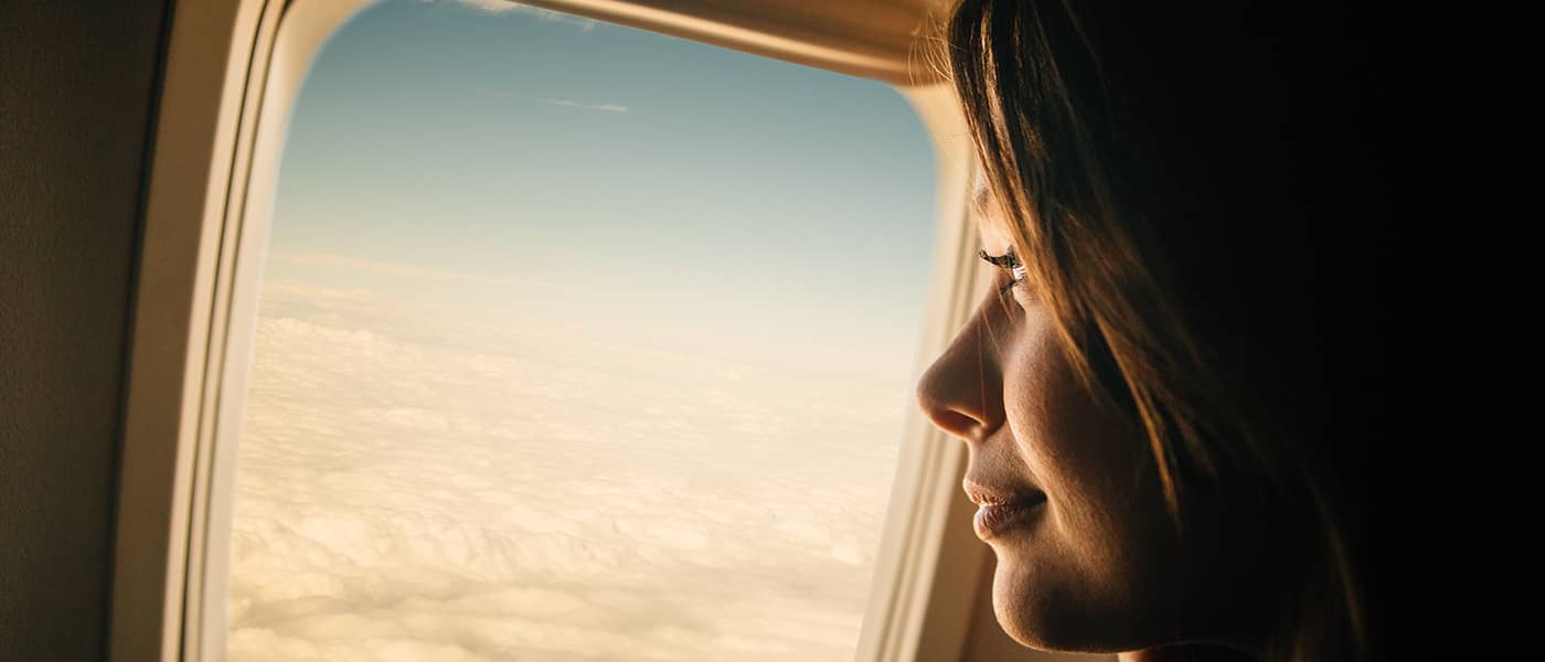 Een vrouw kijkt glimlachend uit het vliegtuigraam